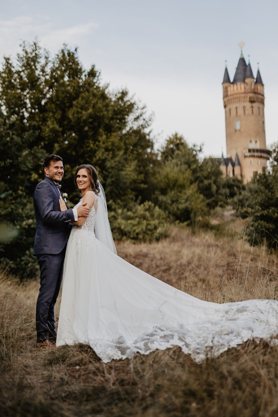 Lachendes Hochzeitspaar in der Natur vor einem Turm