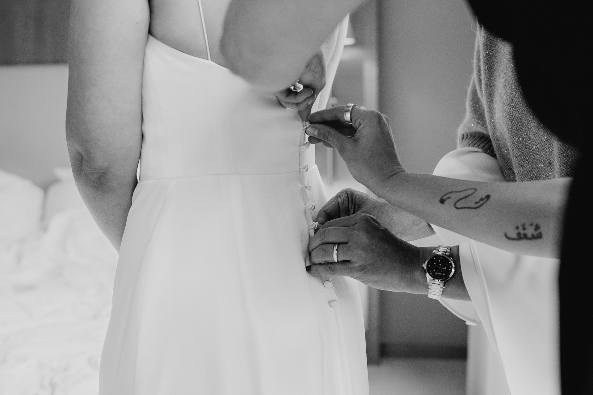 Getting Ready für die Hochzeit: Braut beim Ankleiden. Stylistin hilft ihr mit dem Rückenverschluss des Brautkleids. Foto in schwarz-weiß von Laura-Sophie Jung.
