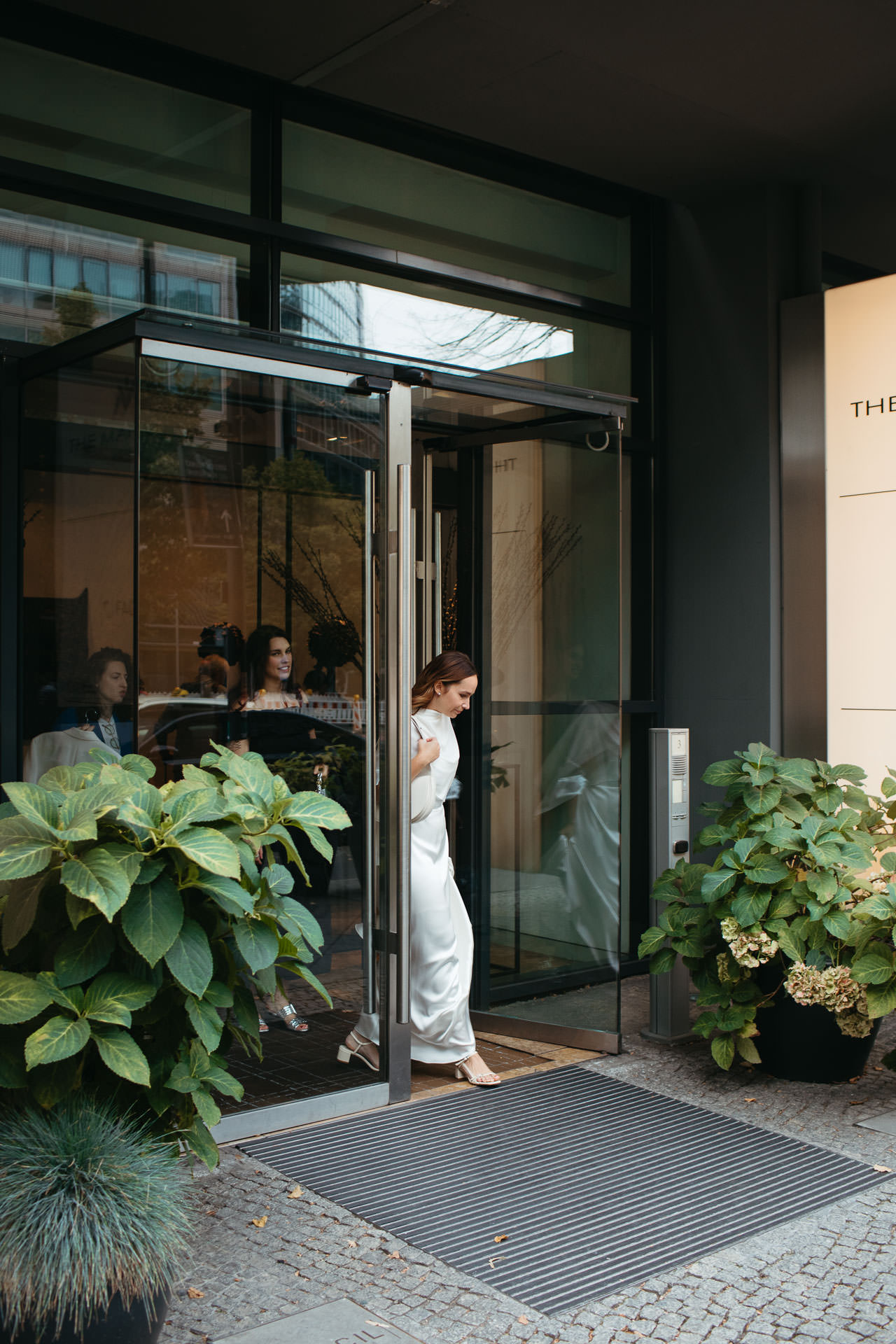 Vor der Hochzeit: Braut im Hochzeitskleid auf dem Weg zur Trauung geht durch eine Drehtür ins Freie. Foto von Laura-Sophie Jung.