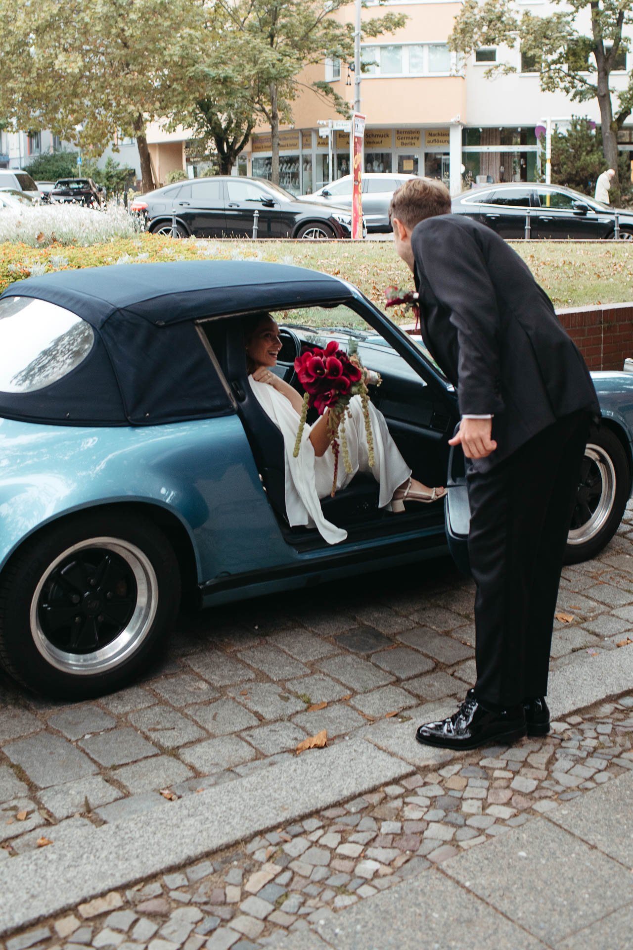 Ankunft beim Standesamt: Bräutigam empfängt Braut, die aus dem Hochzeitsauto aussteigt. Foto von Laura-Sophie Jung, Hochzeitsfotografin Berlin.