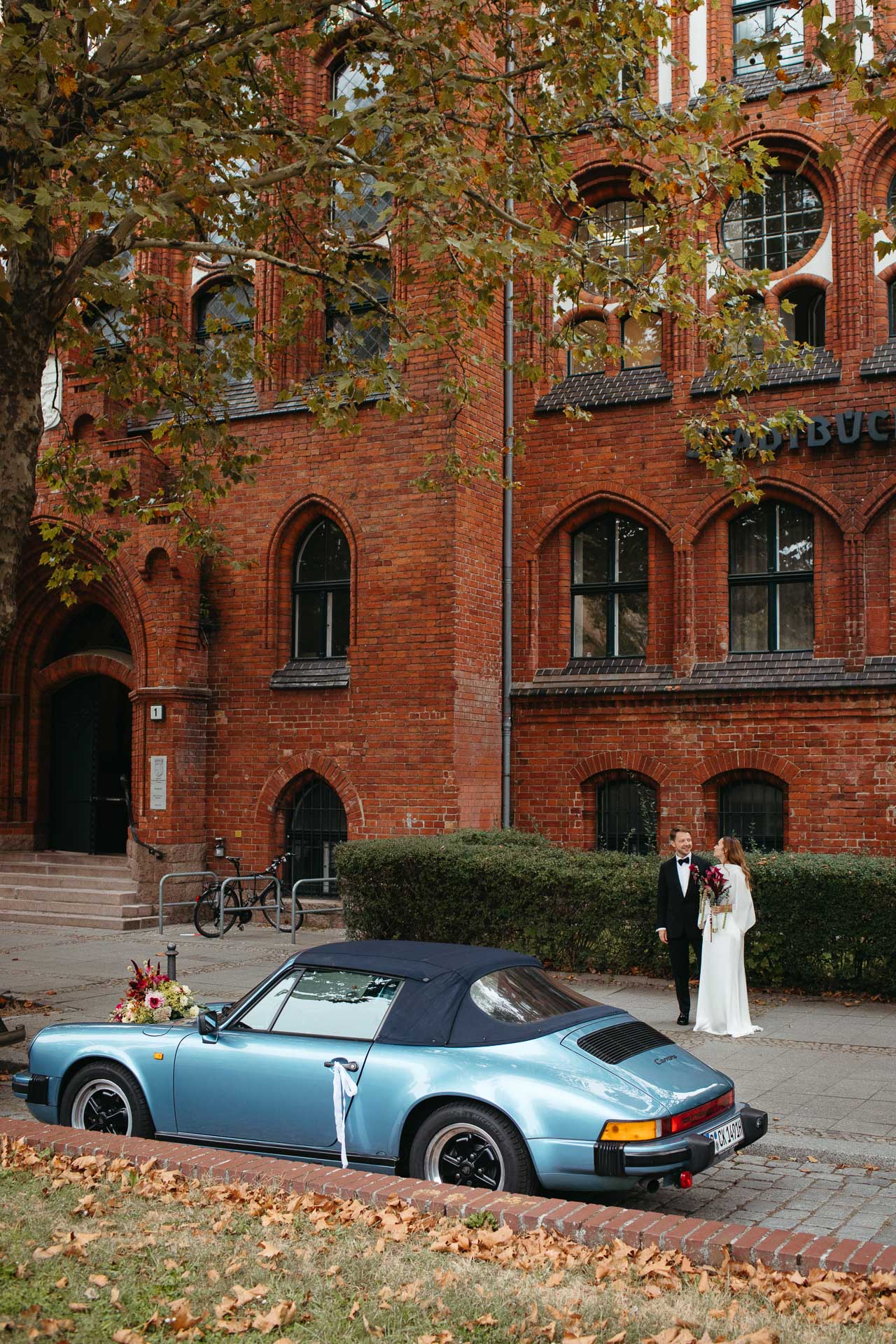 Braut, Bräutigam und Hochzeitsauto vor dem Rathaus Schmargendorf. Bild von Laura-Sophie Jung, Hochzeitsfotografin Berlin.