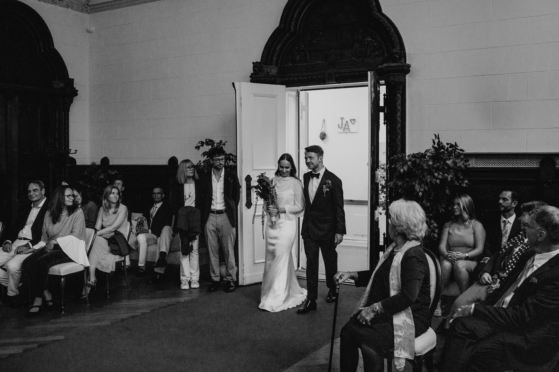 Braut und Bräutigam betreten gemeinsam den Trausaal im Standesamt Schmargendorf in Berlin. Foto in schwarz-weiß von Laura-Sophie Jung.