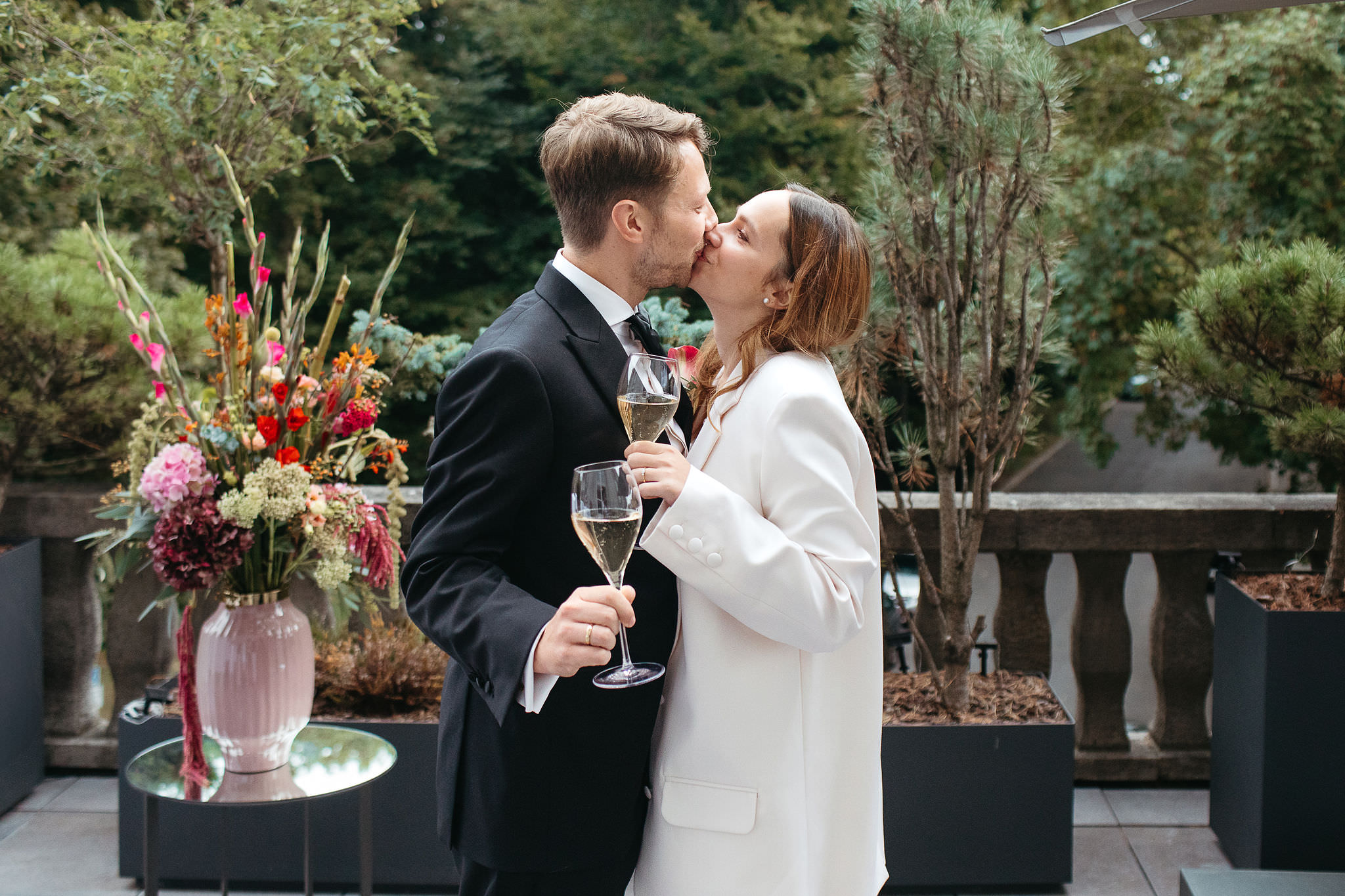 Glückliches Brautpaar bei der Hochzeitsfeier: Braut und Bräutigam küssen sich, beide mit Sektglas. Fotografiert von Laura-Sophie Jung.