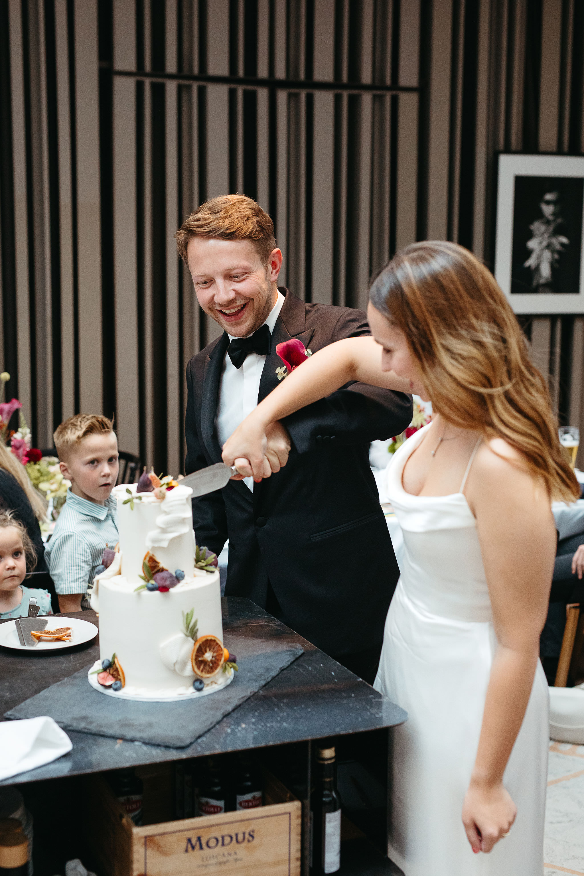 Während der Hochzeitsfeier: Brautpaar schneidet fröhlich lachend gemeinsam die Hochzeitstorte an. Fotografiert von Laura-Sophie Jung, Hochzeitsfotografin Berlin.