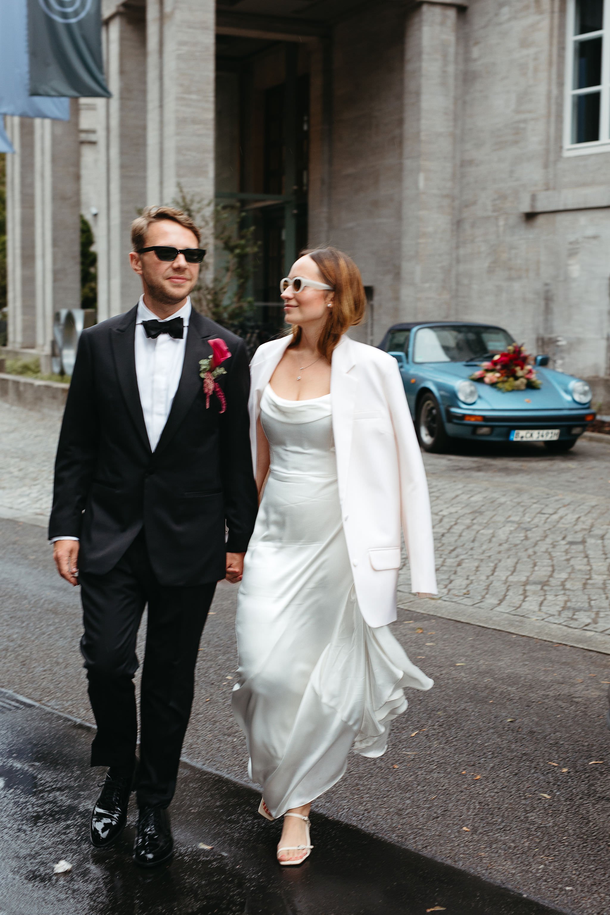 Hochzeitsshooting trotz Regen: Brautpaar mit Hochzeitsauto im Hintergrund. Bild von Laura-Sophie Jung, Hochzeitsfotografin Berlin.