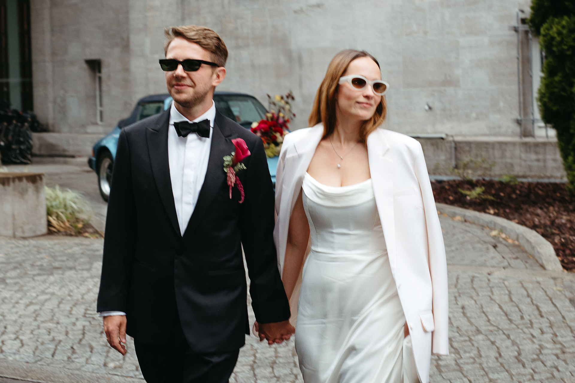 Hochzeitsshooting: Brautpaar Hand in Hand, Hochzeitsauto im Hintergrund. Bild von Laura-Sophie Jung, Hochzeitsfotografin Berlin.