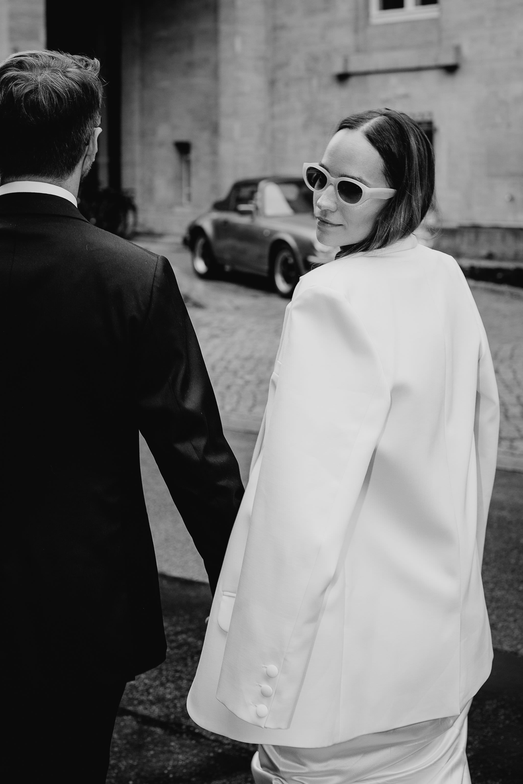 Hochzeits-Fotoshooting: Brautpaar post mit Porsche Oldtimer Hochzeitsauto im Hintergrund. Bild in schwarz-weiß von Laura-Sophie Jung, Hochzeitsfotografin Berlin.