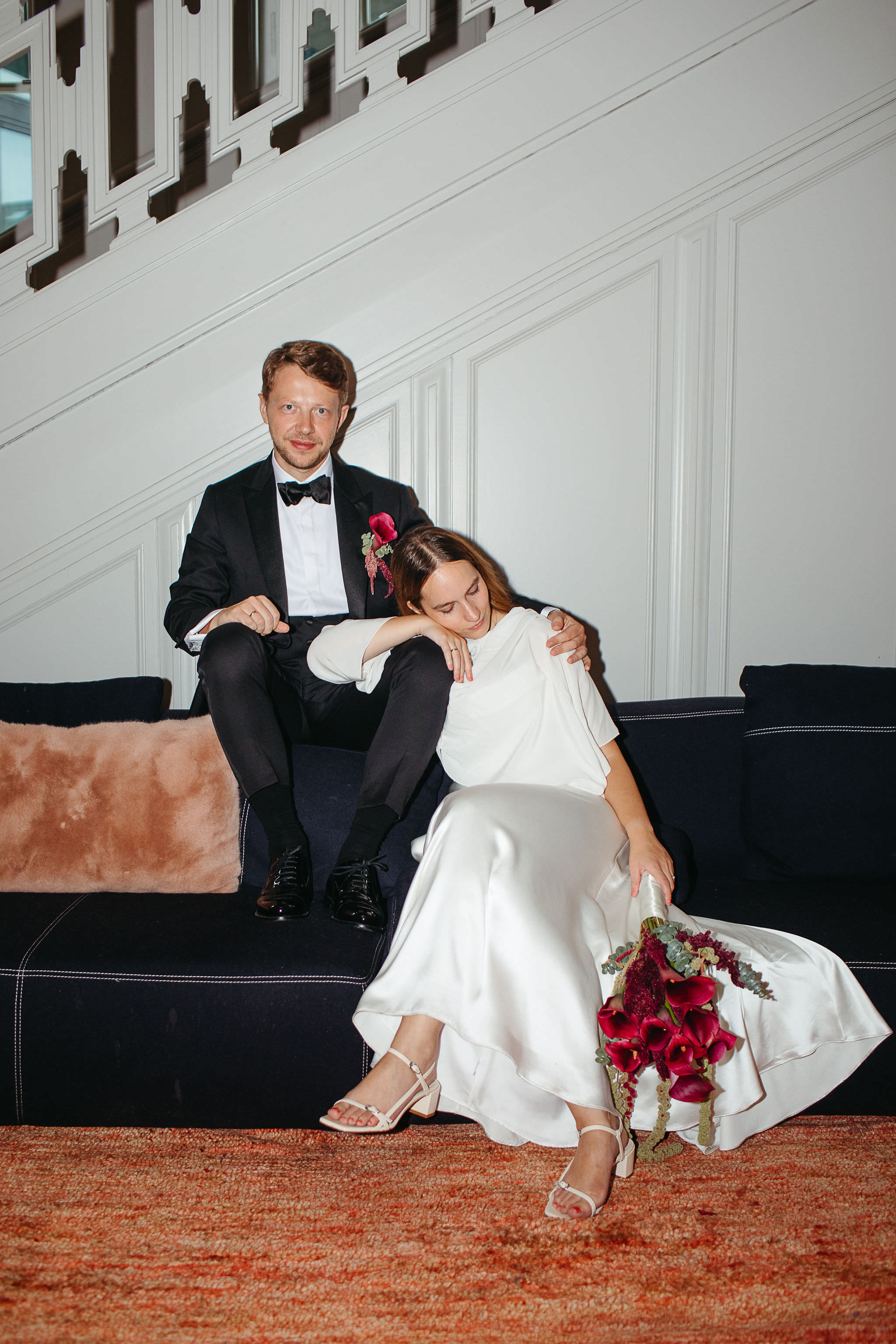Ein emotionaler Tag geht zu Ende: Erschöpftes Brautpaar auf einem Sofa, Braut lehnt sich müde an Bräutigam an. Fotografiert von Laura-Sophie Jung, Hochzeitsfotografin Berlin.