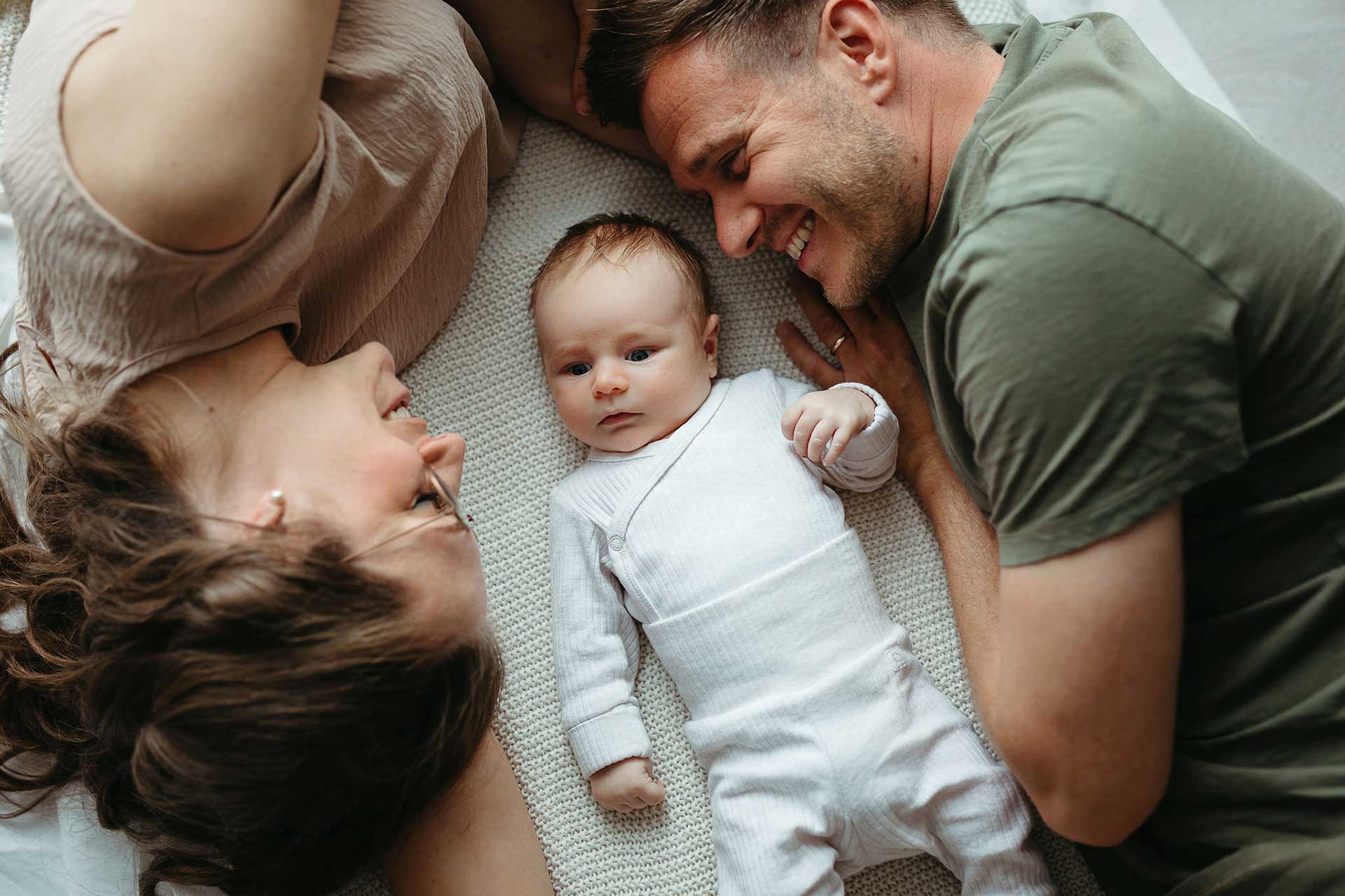 Entspanntes Familienfoto Zuhause: Mama, Papa und Baby liegend von oben fotografiert. Bild von Laura-Sophie Jung.