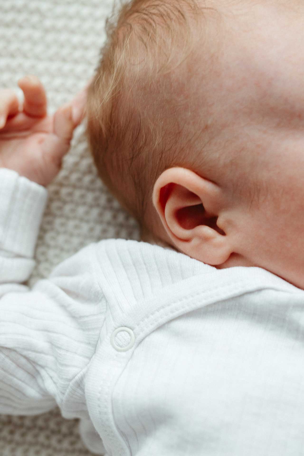 Familien-Homestory: Detailansicht vom Kopf des Babys mit Ohr und Hand über dem Kopf. Fotografiert von Laura-Sophie Jung.