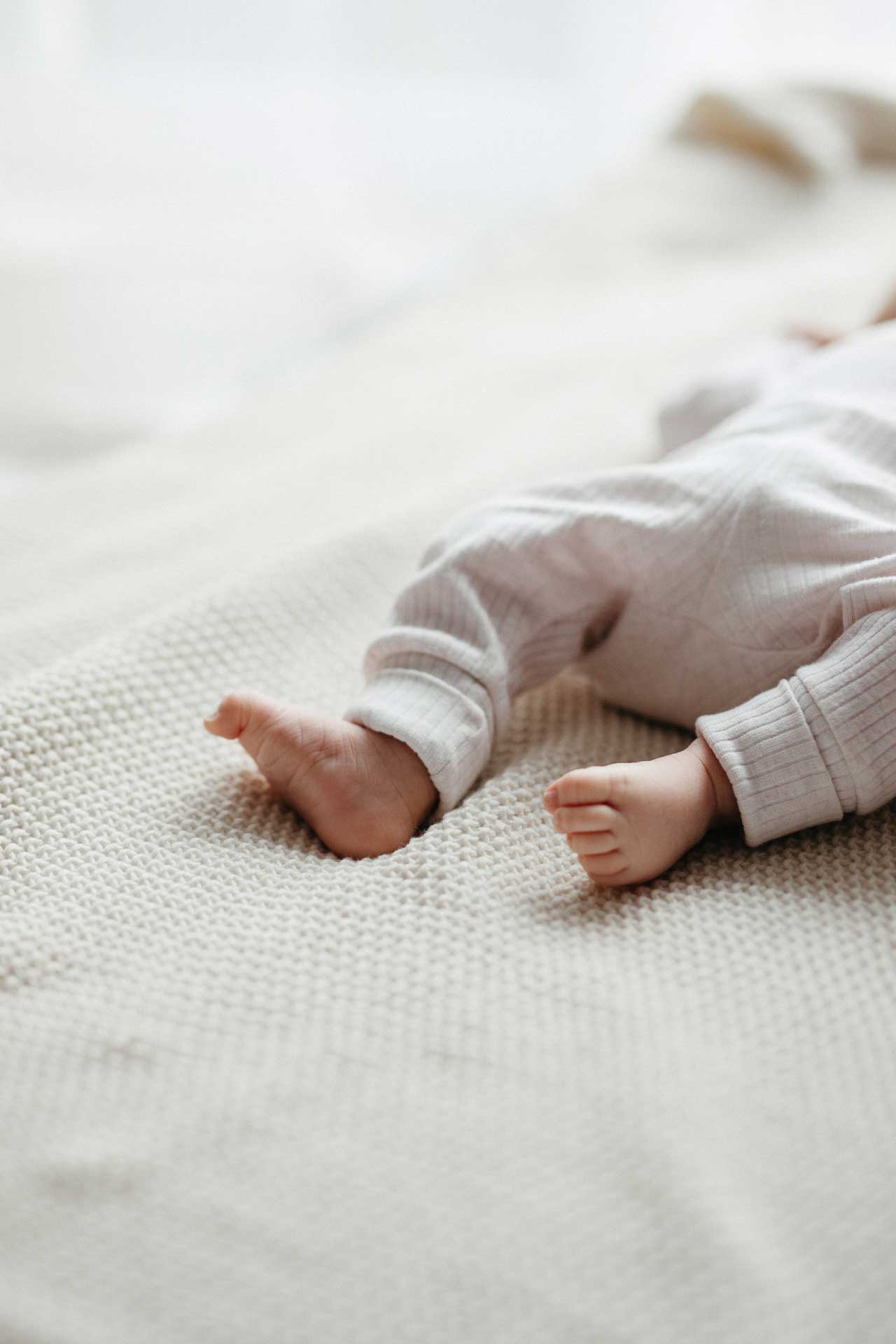 Entspannte Familienfotos zu Hause: Baby liegt auf einer Decke, die kleinen Füße im Fokus des Bildes. Fotografiert von Laura-Sophie Jung.