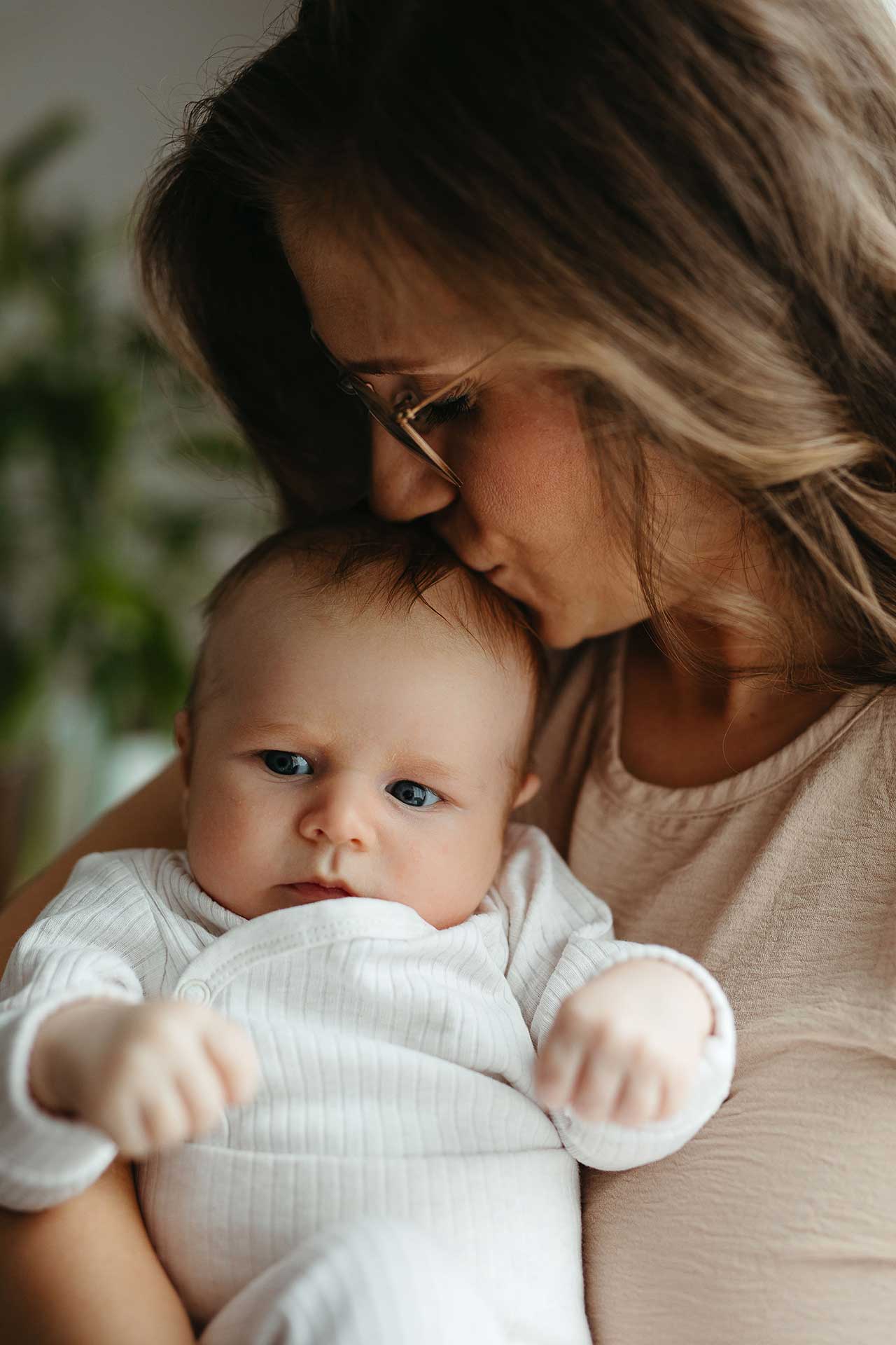 Authentische Familienfotos zu Hause: Mama hält Baby auf dem Arm und gibt ihm einen Kuss auf den Kopf. Fotografiert von Laura-Sophie Jung.