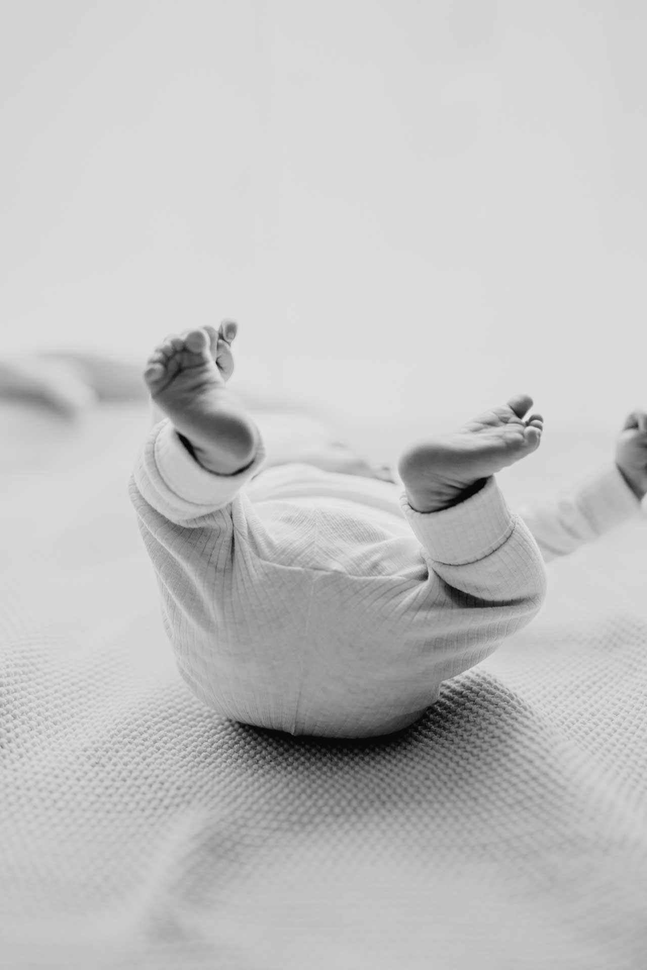 Babyfoto in schwarz-weiß: Baby liegt auf dem Rücken und streckt die Beine in die Luft. Fotografiert von Laura-Sophie Jung.