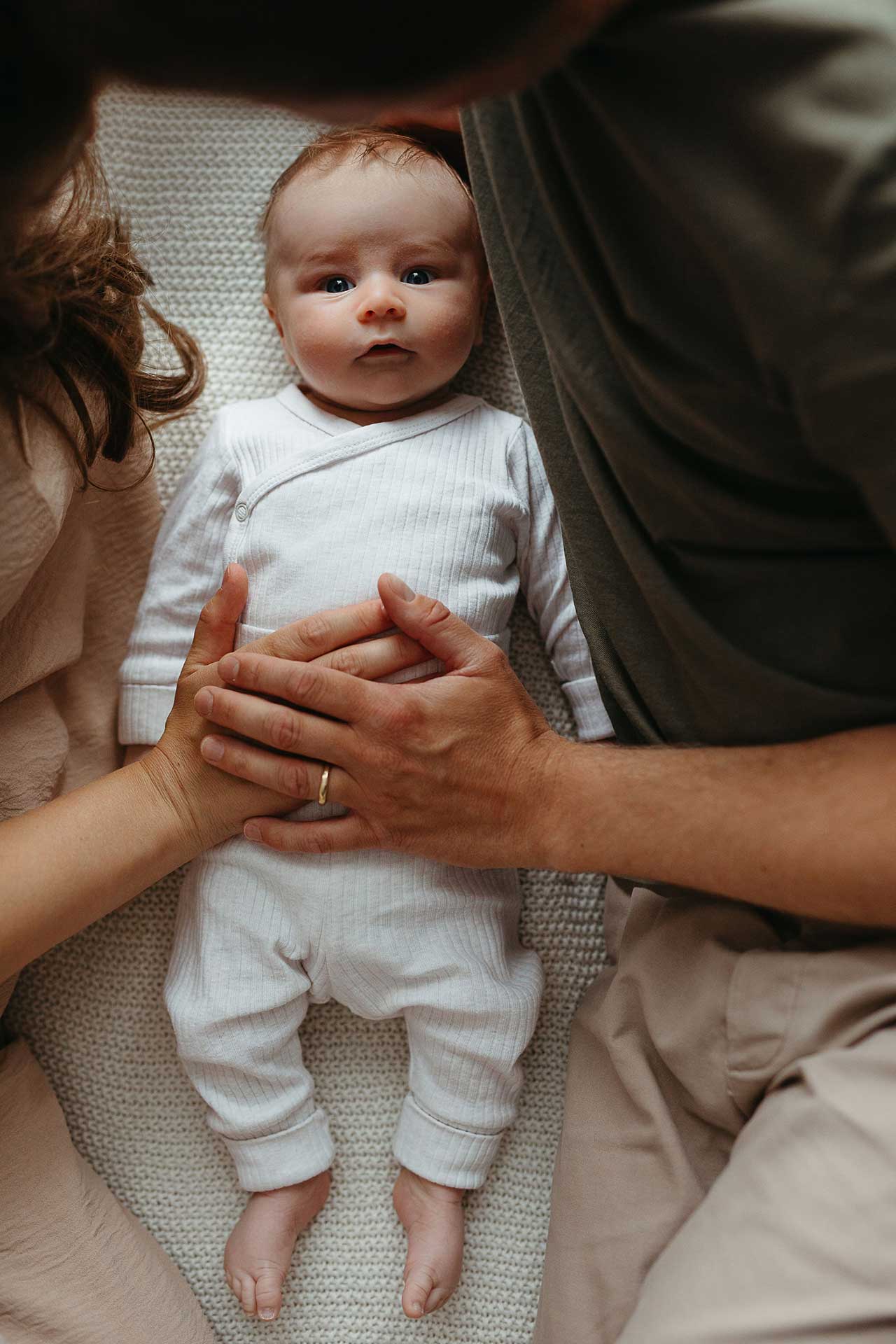 Entspannte Familienfotos zu Hause: Mutter, Vater und Baby liegen auf einer Decke, die Eltern haben je eine Hand auf dem Bauch des Babys. Fotografiert von Laura-Sophie Jung.