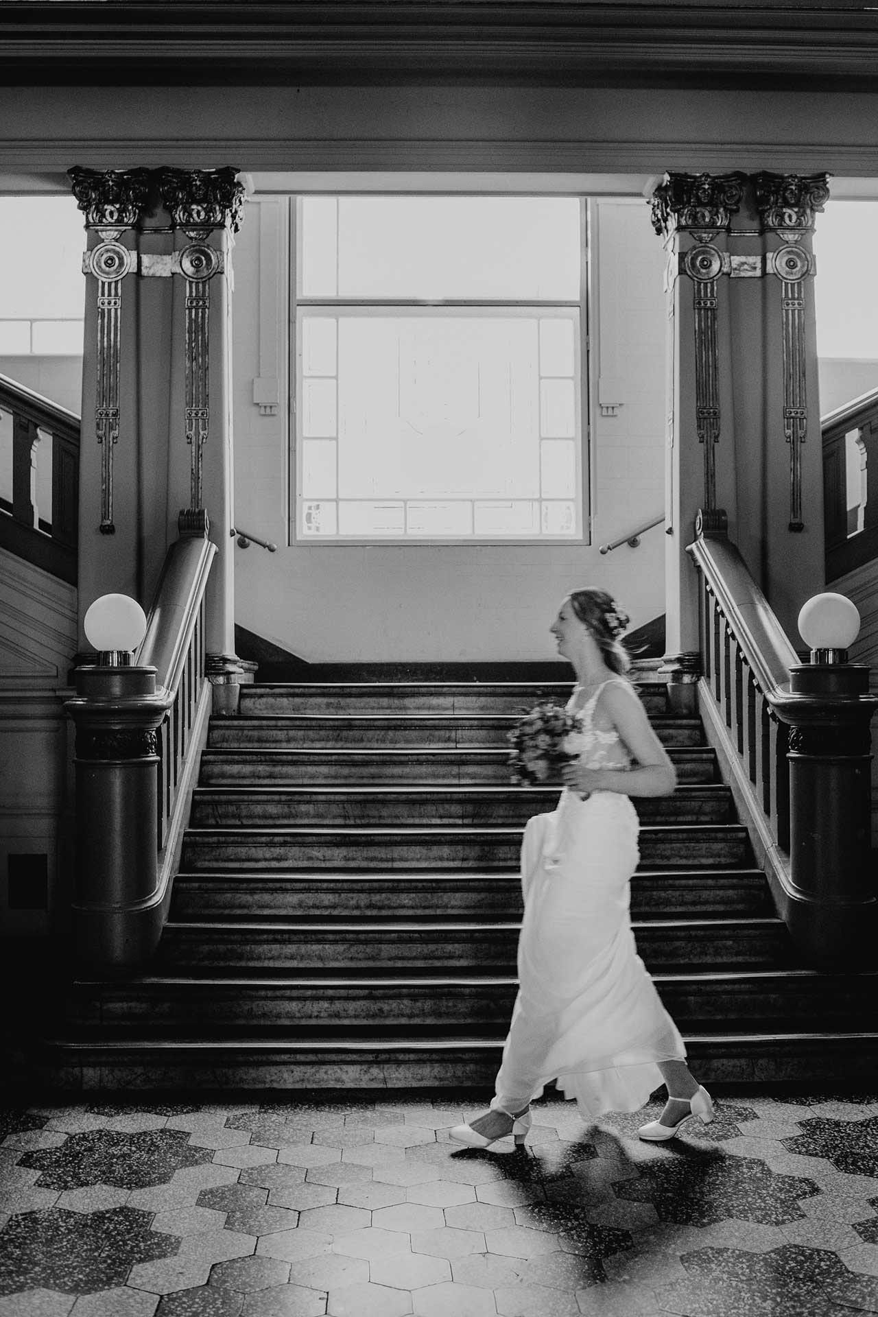 Hochzeitsfotos Standesamt: Braut rennt glücklich durch das Treppenhaus. Fotografiert von Laura-Sophie Jung