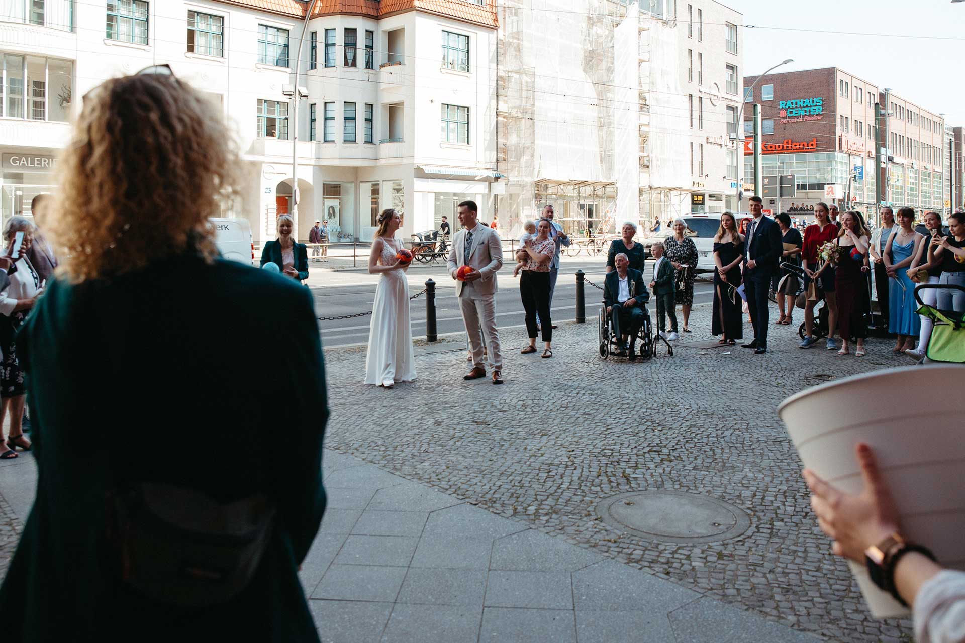 Hochzeitsfotos Standesamt: Menschen stehen auf Platz und blicken auf Brautpaar. Fotografiert von Laura-Sophie Jung