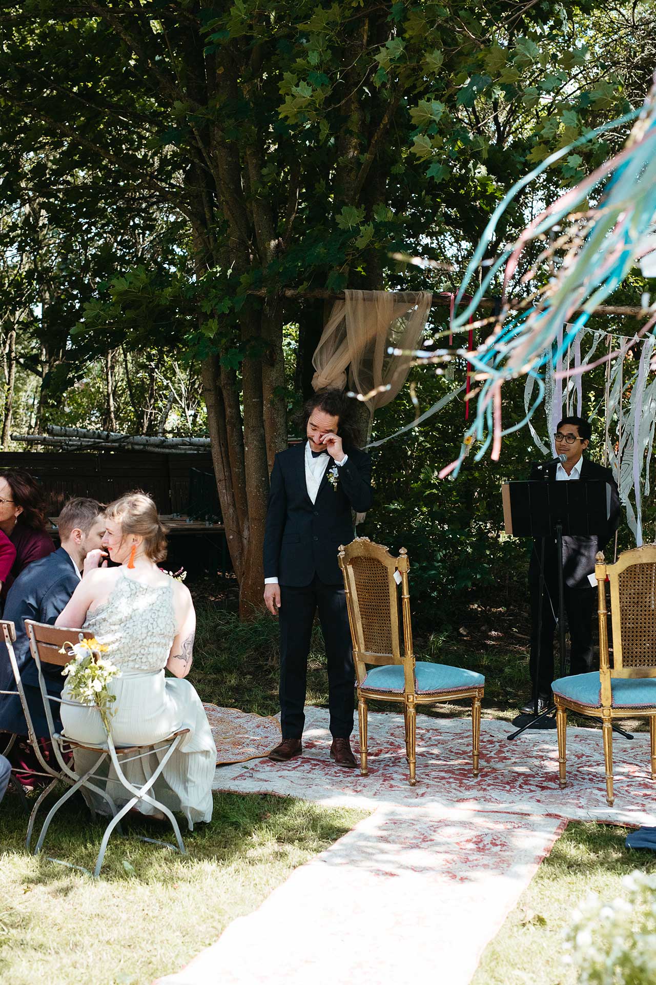 Natürliche Hochzeitsfotos: Bräutigam zeigt Emotionen und wischt sich eine Träne aus dem Auge, während er die Ankunft der Braut zur Trauung erwartet. Foto von Laura-Sophie Jung.