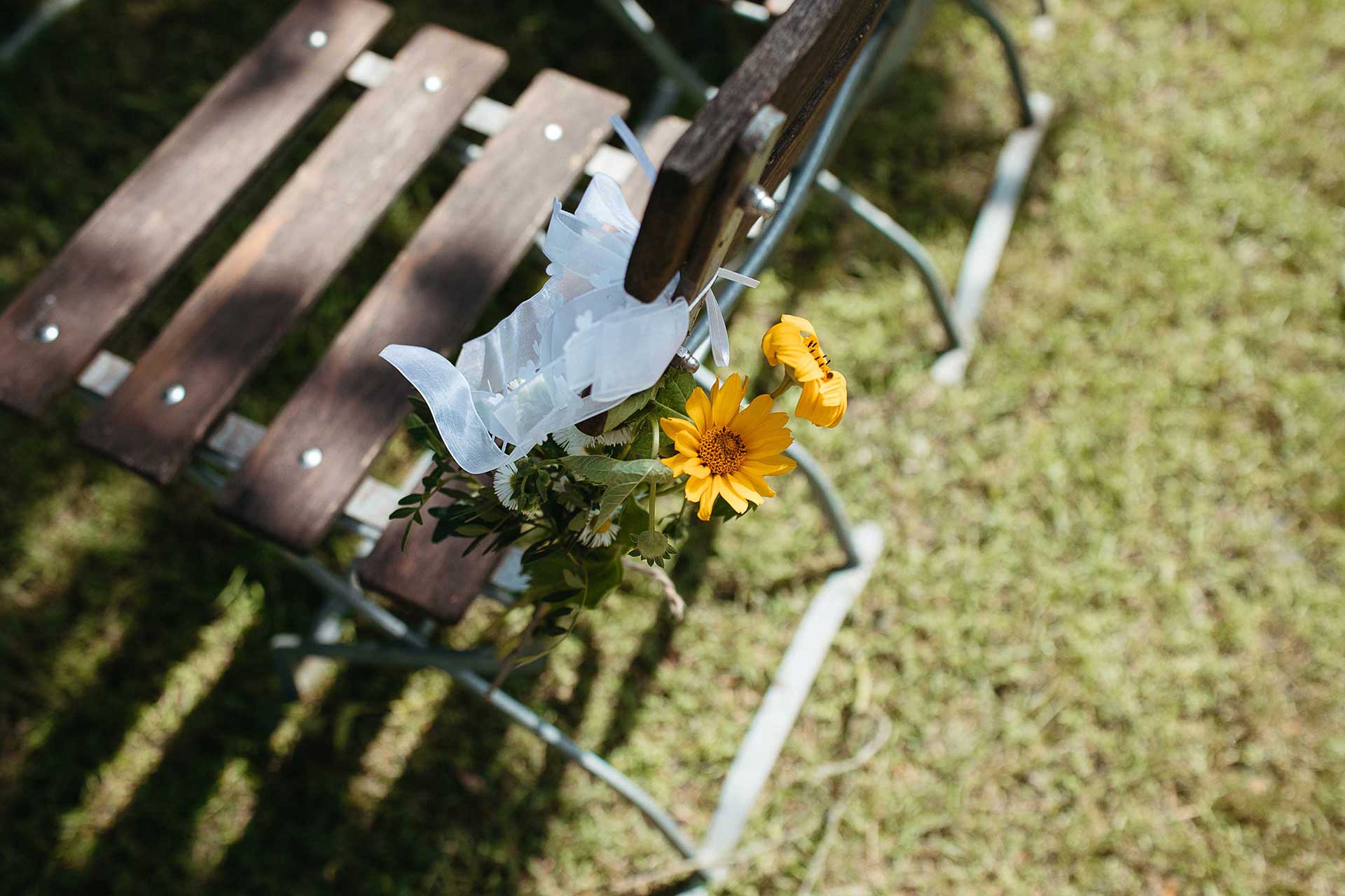 Hochzeitsreportage in Brandenburg auf dem Land: Rustikale Blumendekoration an einem Gartenstuhl. Foto von Laura-Sophie Jung.