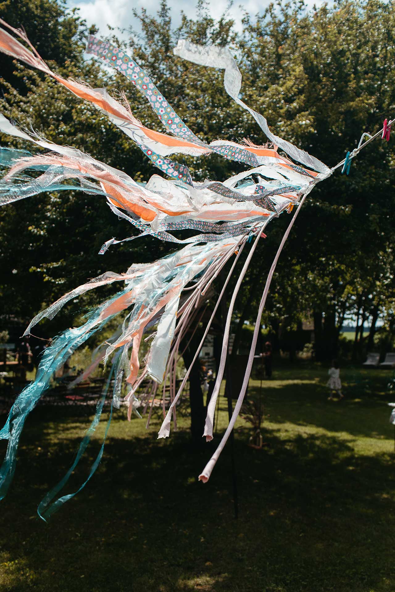 Festivalhochzeit in Brandenburg auf dem Land: Wehende Dekoration mit bunten Bändern im Garten der Hochzeitslocation. Foto von Laura-Sophie Jung.