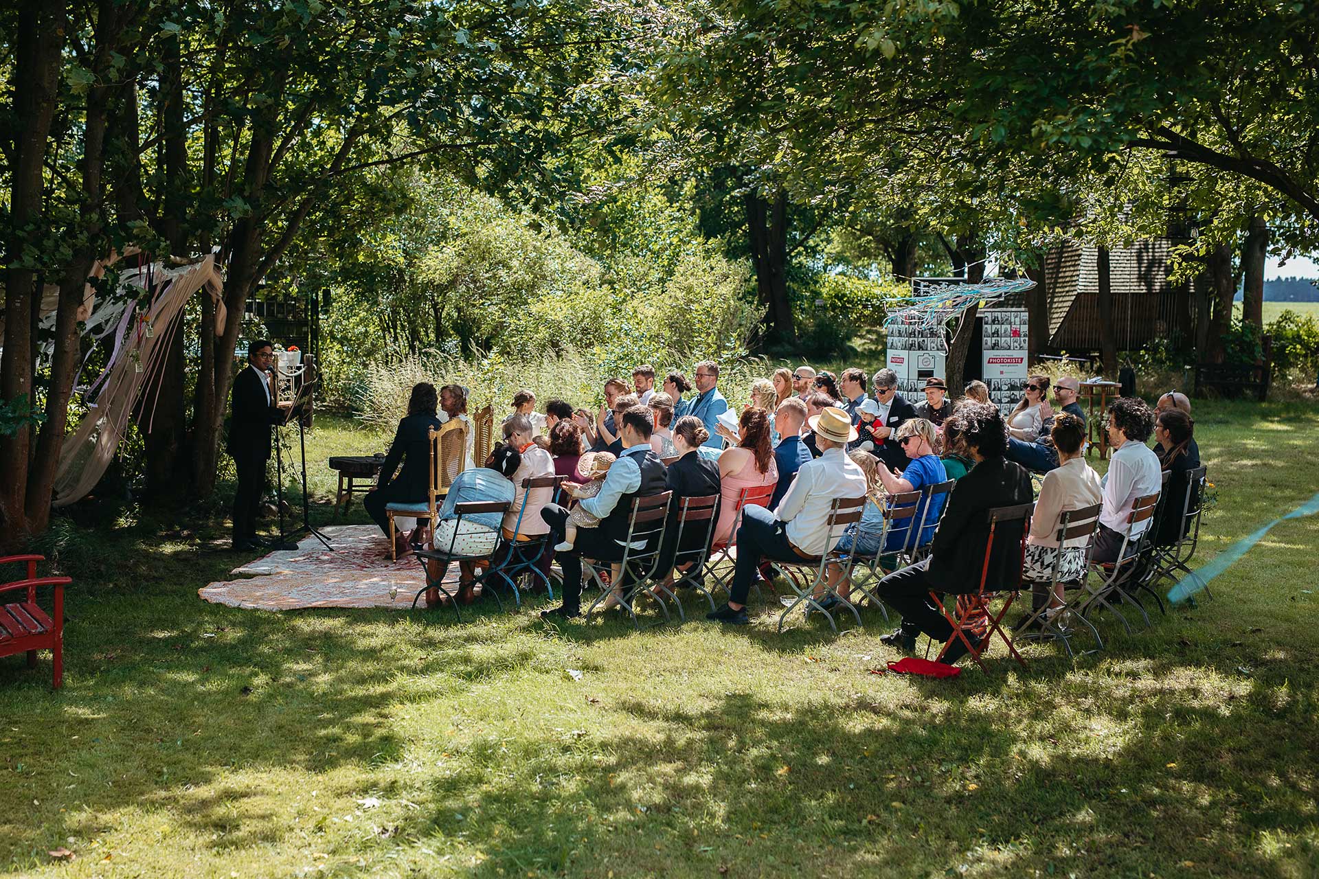 Festivalhochzeit auf dem Land in Brandenburg: Brautpaar und Gäste während der Zeremonie im Garten der Location. Foto von Laura-Sophie Jung.