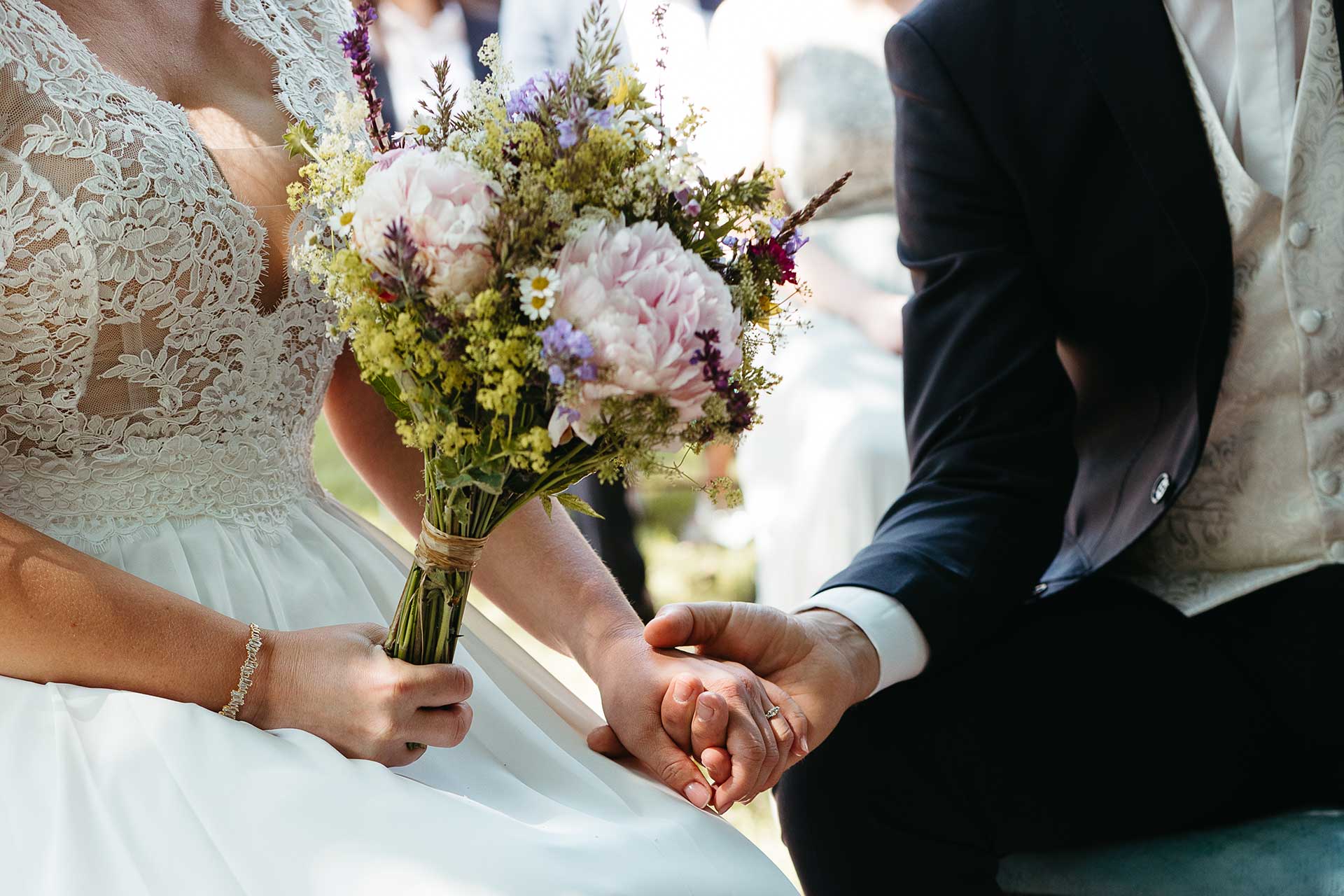 Hochzeitsfoto: Braut und Bräutigam halten sich während der Zeremonie an der Hand, die Braut hält in der anderen Hand den Brautstrauß aus frischen Wiesenblumen. Fotografiert von Laura-Sophie Jung, Hochzeitsfotografin Berlin, Brandenburg & deutschlandweit.
