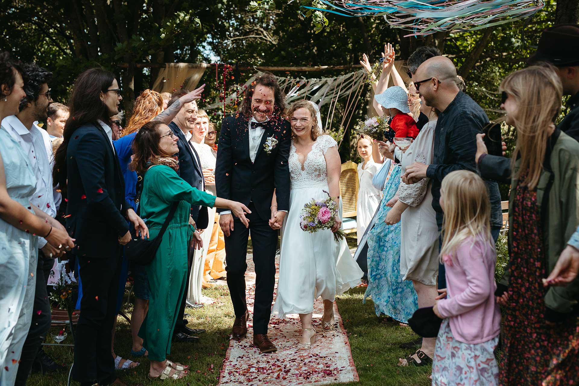 Heiraten auf dem Land in Brandenburg: Das glückliche Brautpaar beim Auszug nach der Trauung. Gäste werfen Konfetti. Foto von Laura-Sophie Jung.