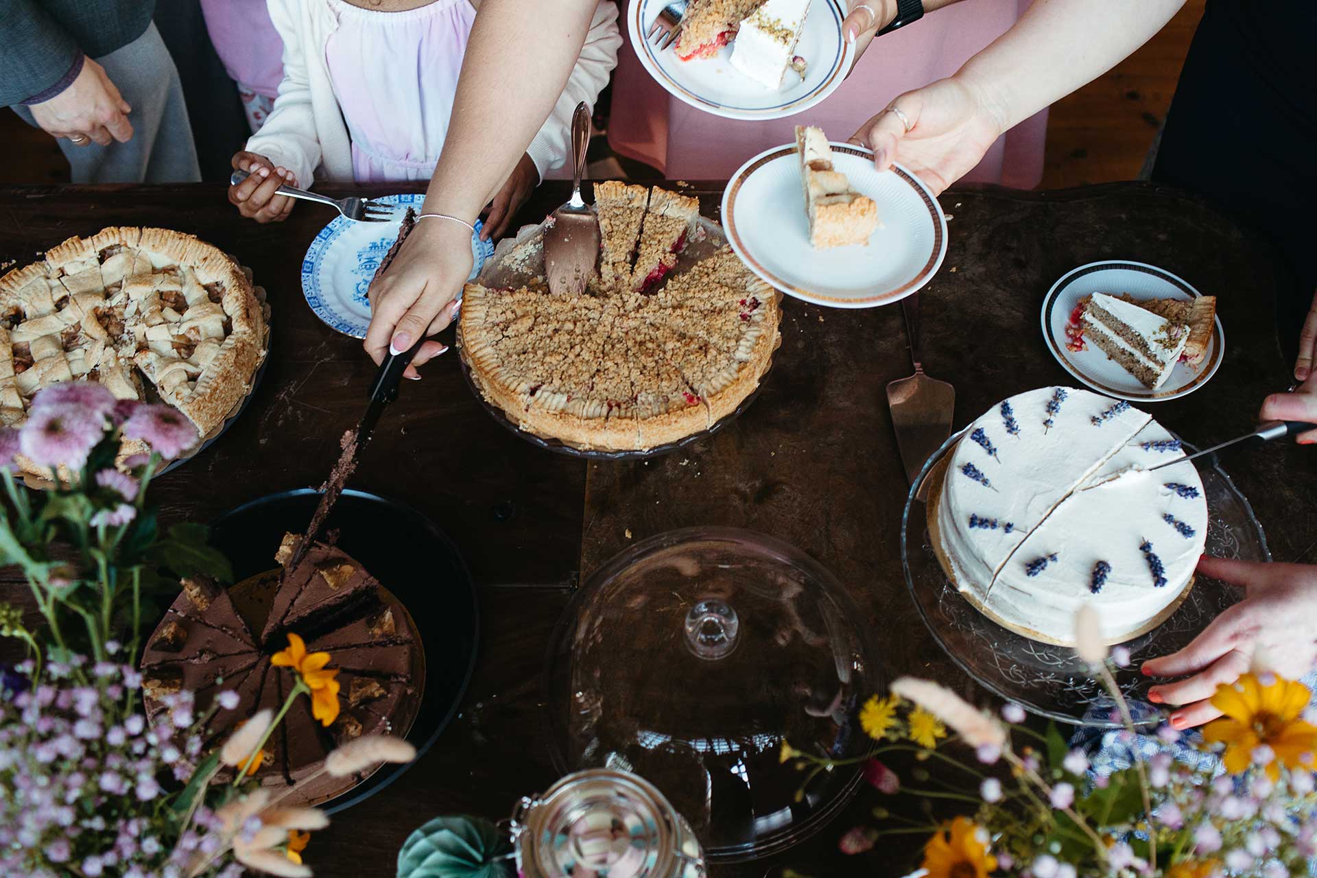 Hochzeit auf dem Land: Blick von oben auf das Kuchenbuffet auf einem Holztisch angerichtet und liebevoll mit Wiesenblumen dekoriert. Foto von Laura-Sophie Jung.