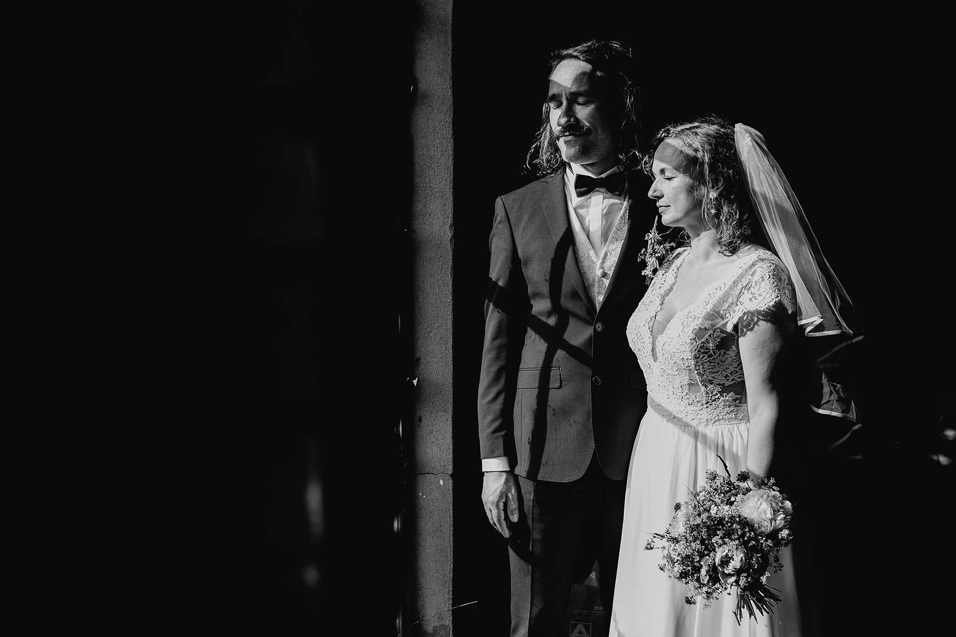 Hochzeitsfoto in schwarz-weiß: Braut und Bräutigam stehen mit geschlossenen Augen im Freien und genießen die Sonne. Fotografiert von Laura-Sophie Jung.