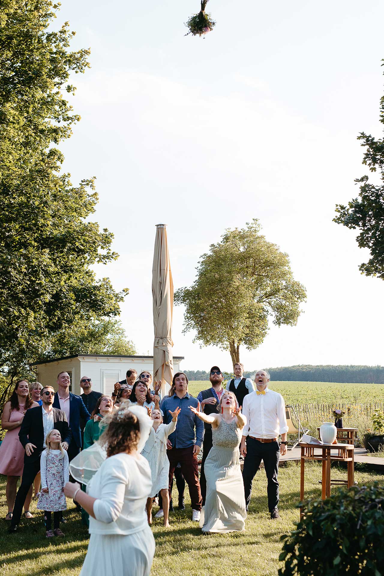 Brautstraußwurf: Braut und Gäste blicken dem fliegenden Strauß hinterher. Foto von Laura-Sophie Jung.