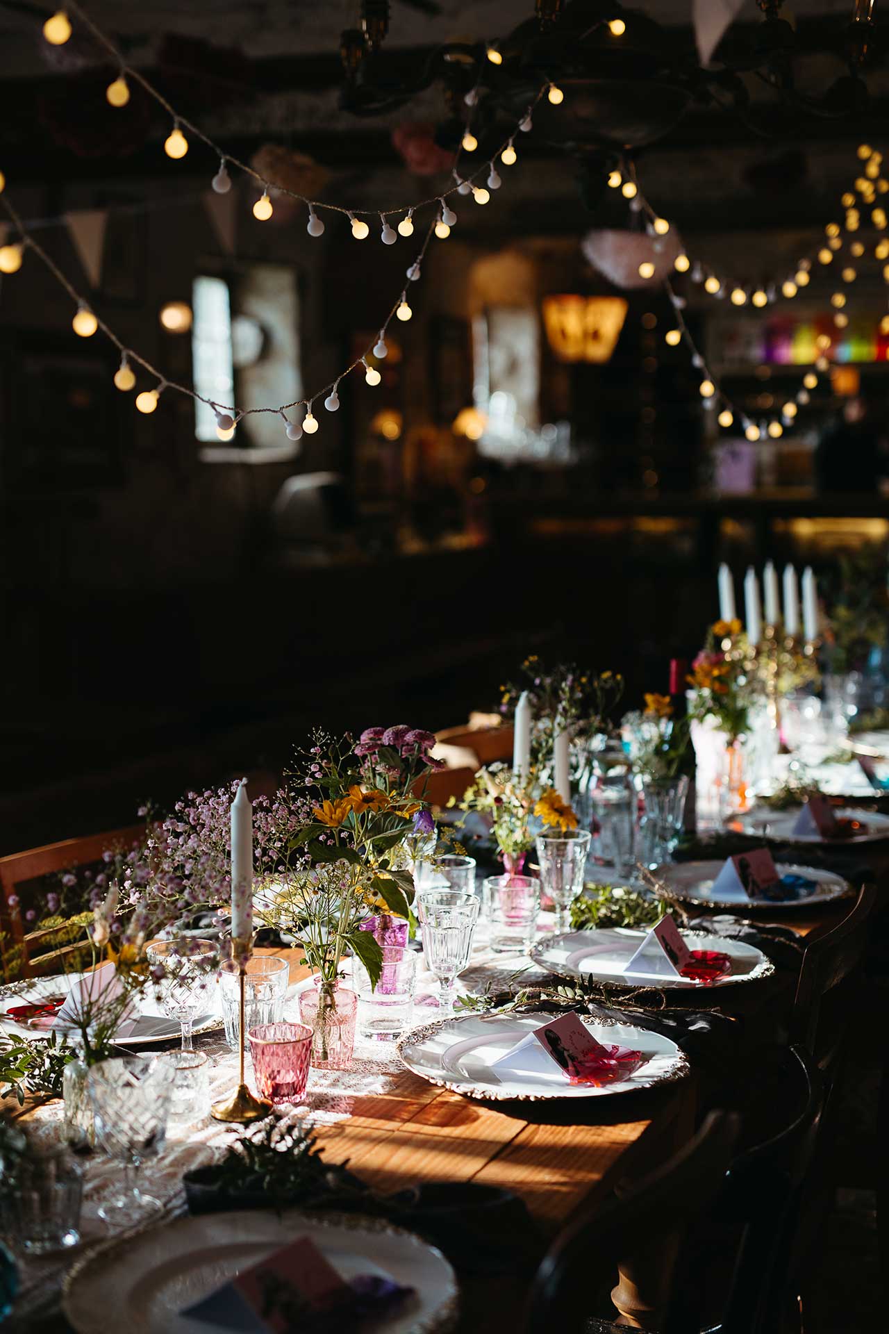 Liebevoll gedeckte Tafel für die Hochzeitsfeier im Freien mit Blumendekoration, Kerzen und Lichterketten. Foto von Laura-Sophie Jung.