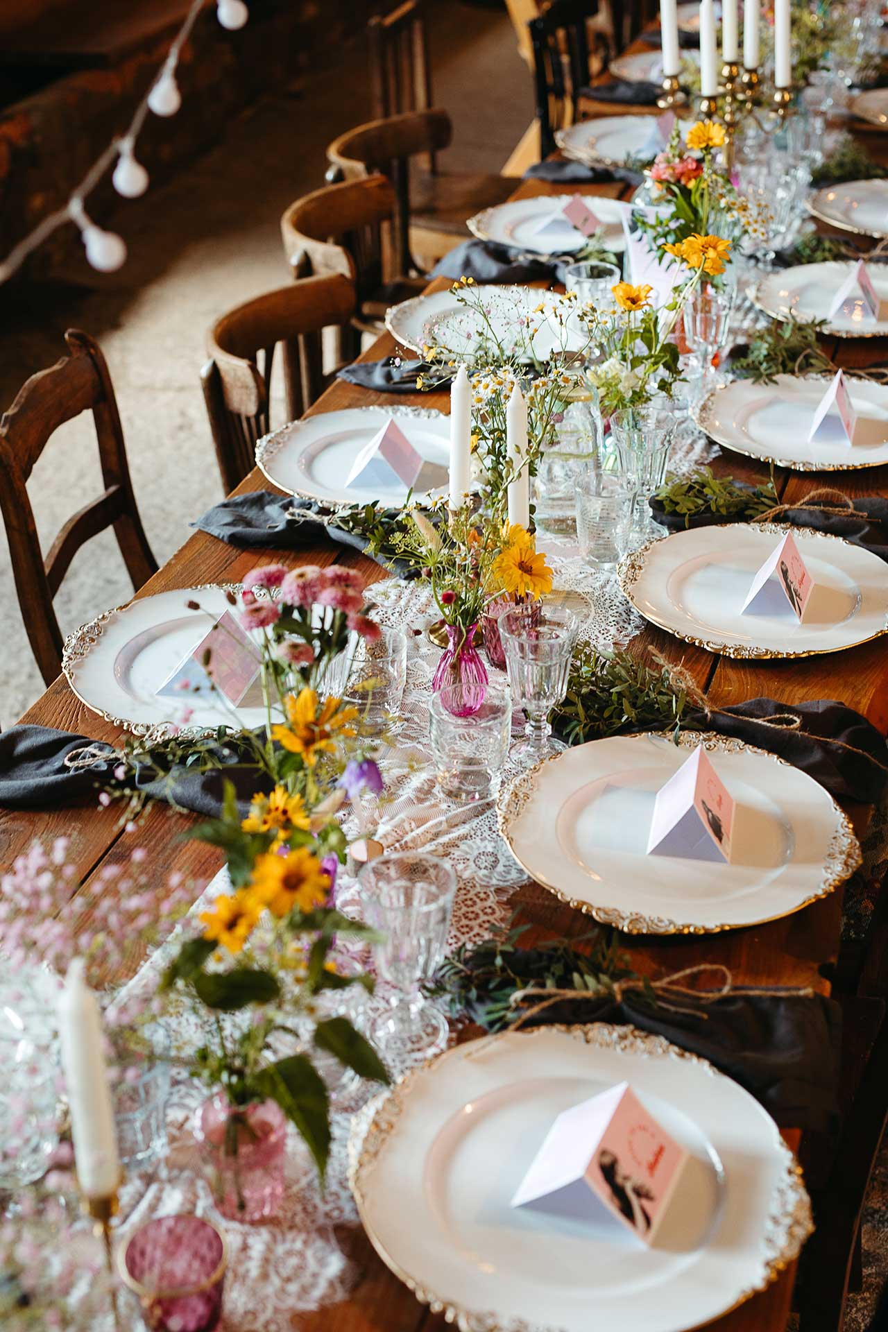 Gedeckte Tafel für die Hochzeitsfeier mit dekorativen Vintage Tellern und Gläsern, Blumen und Kerzen. Foto von Laura-Sophie Jung.