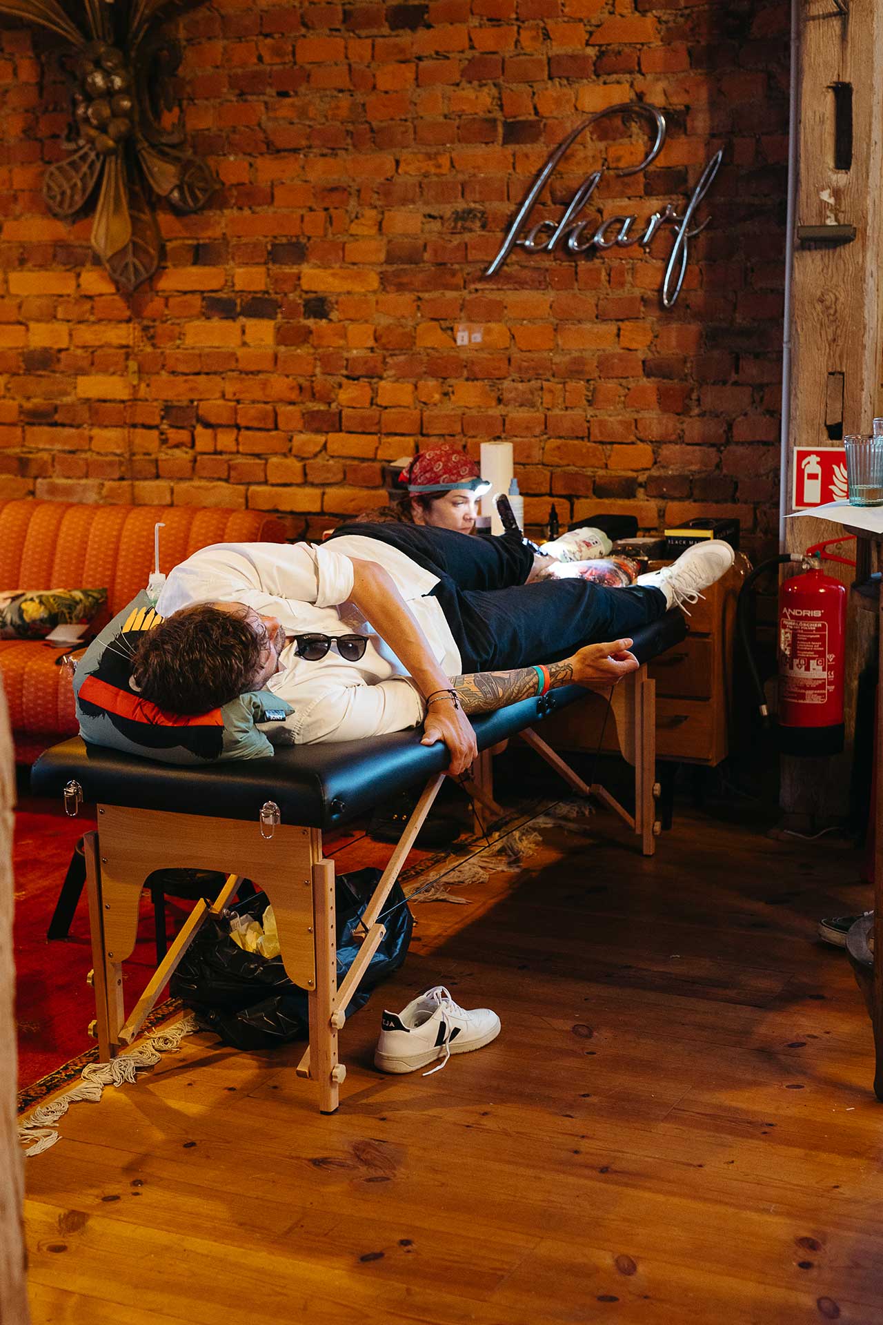Tattoo-Künstlerin tätowiert einen Hochzeitsgast am Fußknöchel. Foto von Laura-Sophie Jung.