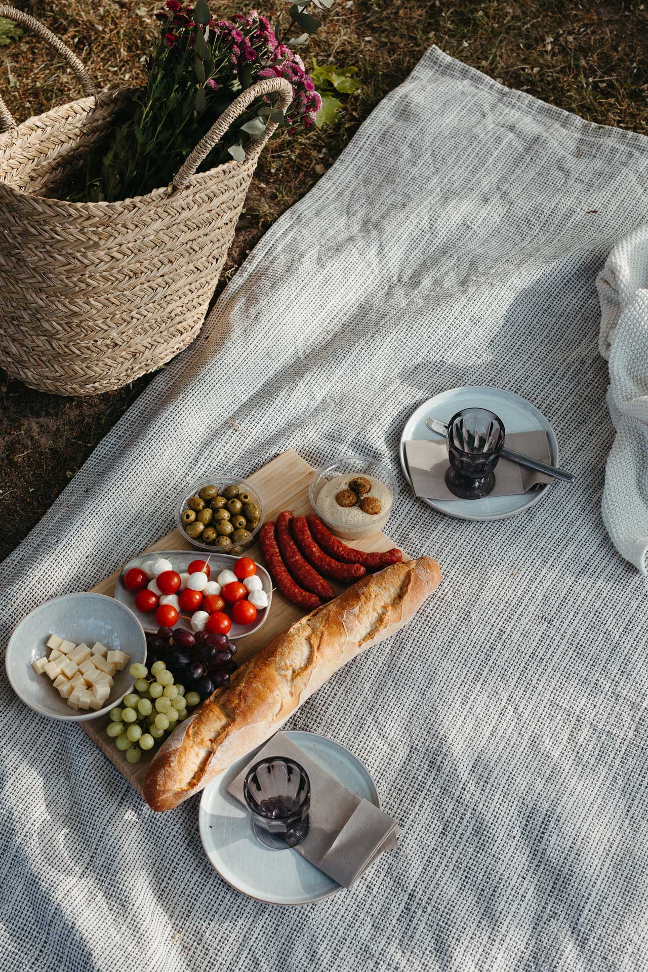 Picknick Date Fotoshooting: Schön angerichtetes Picknick auf einer Decke mit Baguette, Käse, Wurst, Tomaten, Oliven und Hummus. Fotografiert von Laura-Sophie Jung, Berlin.
