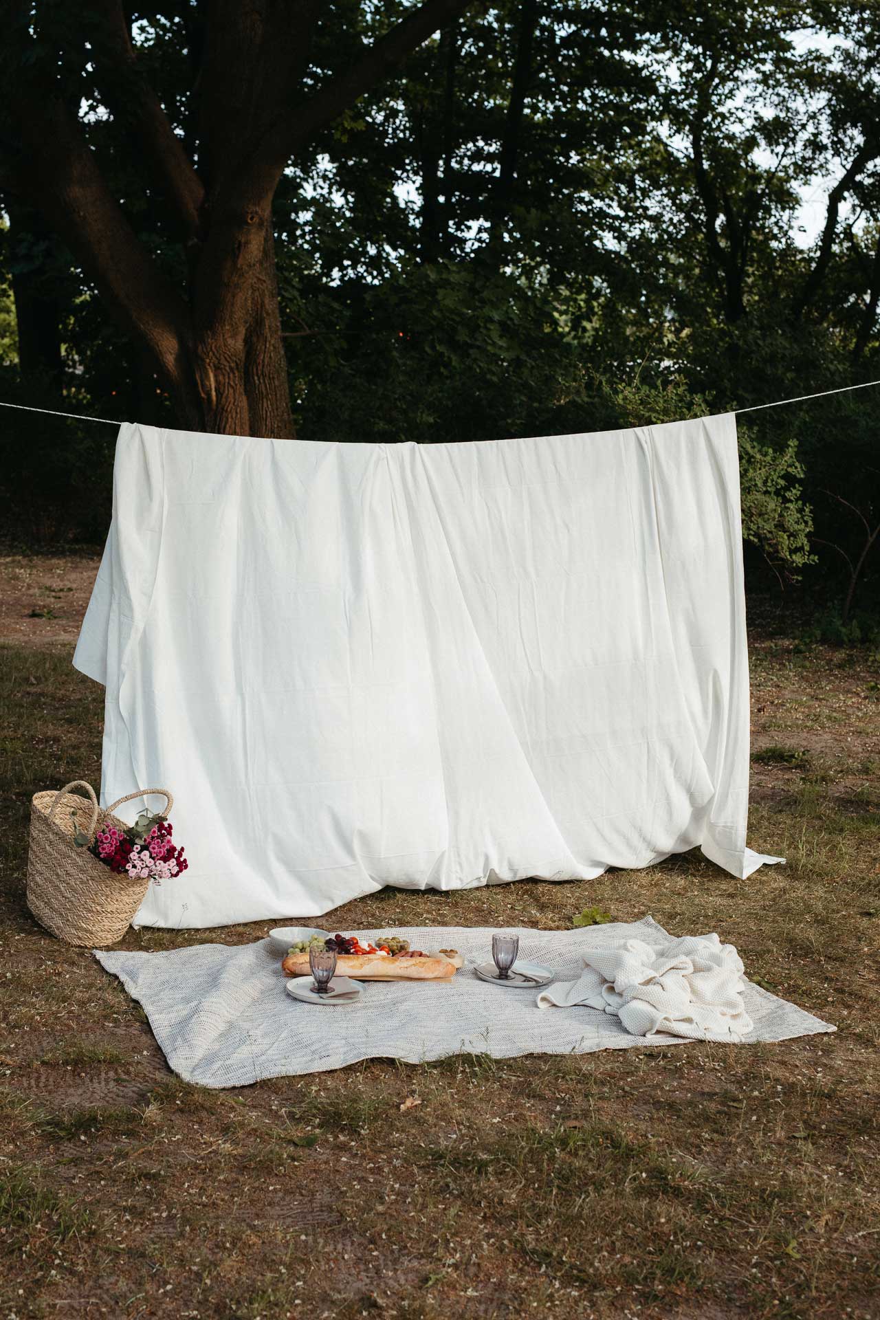Picknick Date Fotoshooting: Schön angerichtetes Picknick auf einer Decke, daneben ein Picknickkorb mit Blumen. Foto von Laura-Sophie Jung, Berlin.
