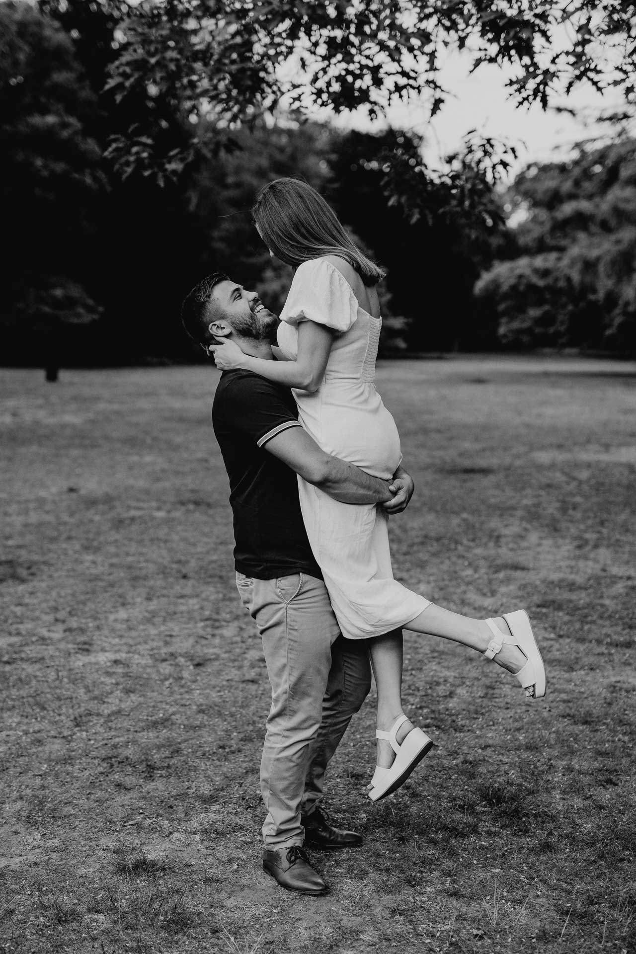 Verlobungsshooting im Park: Mann hebt seine Verlobte hoch, beide schauen sich glücklich verliebt an. Schwarz-weiß Foto von Laura-Sophie Jung, Berlin.