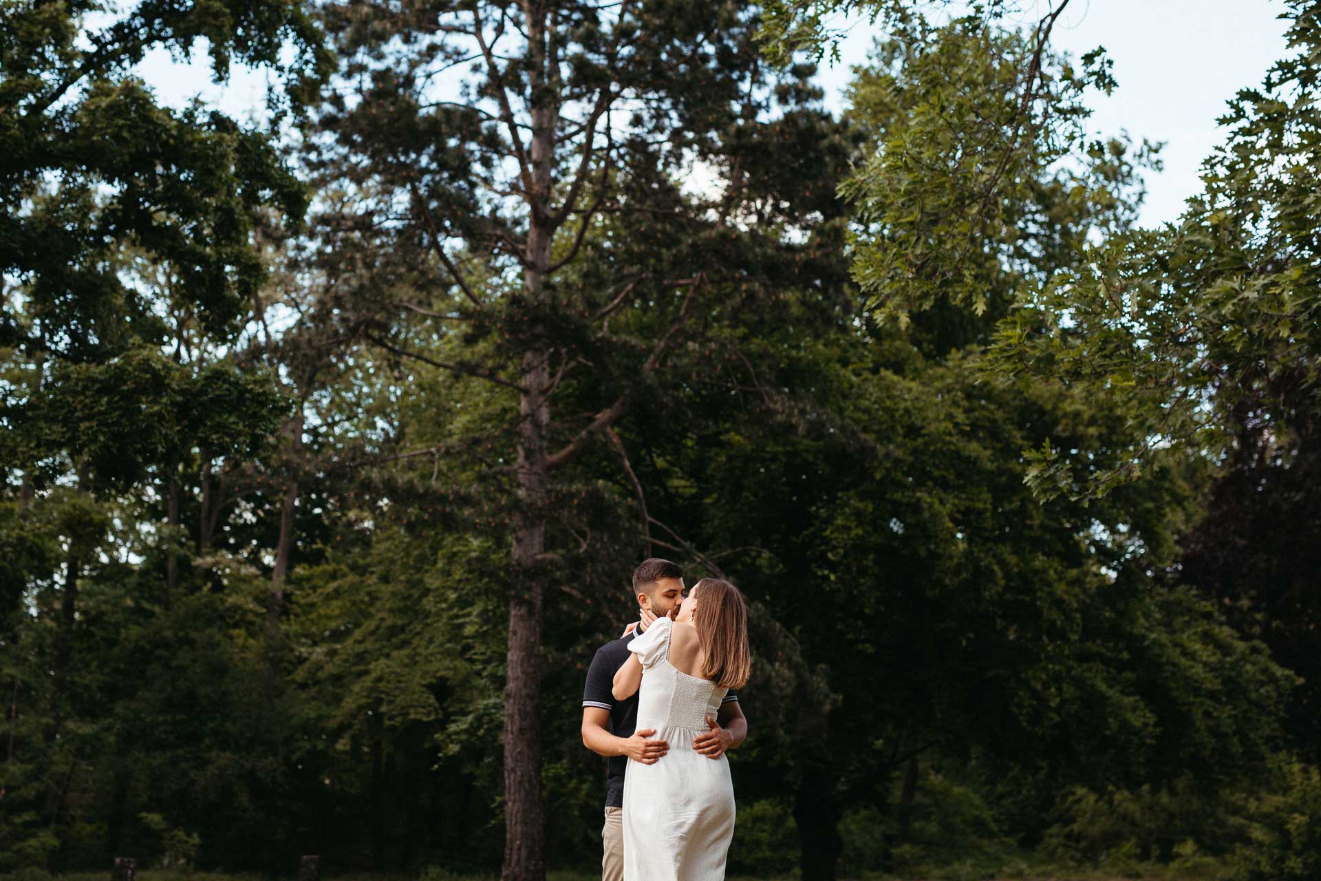 Paar beim Verlobungsshooting outdoor: Mann und Frau umarmen und küssen sich. Im Hintergrund Bäume. Fotografiert von Laura-Sophie Jung, Berlin.