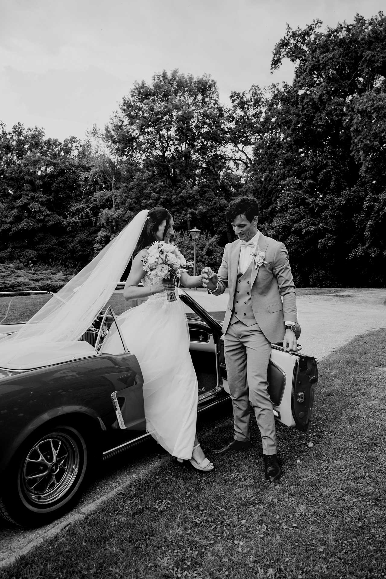 Das Hochzeitspaar steigt aus dem Oldtimer aus – Bräutigam unterstützt die Braut vor dem Seehaus Liebenberg